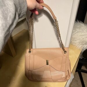 Nude/tan color bow purse with adjustable strap. Gold accents.